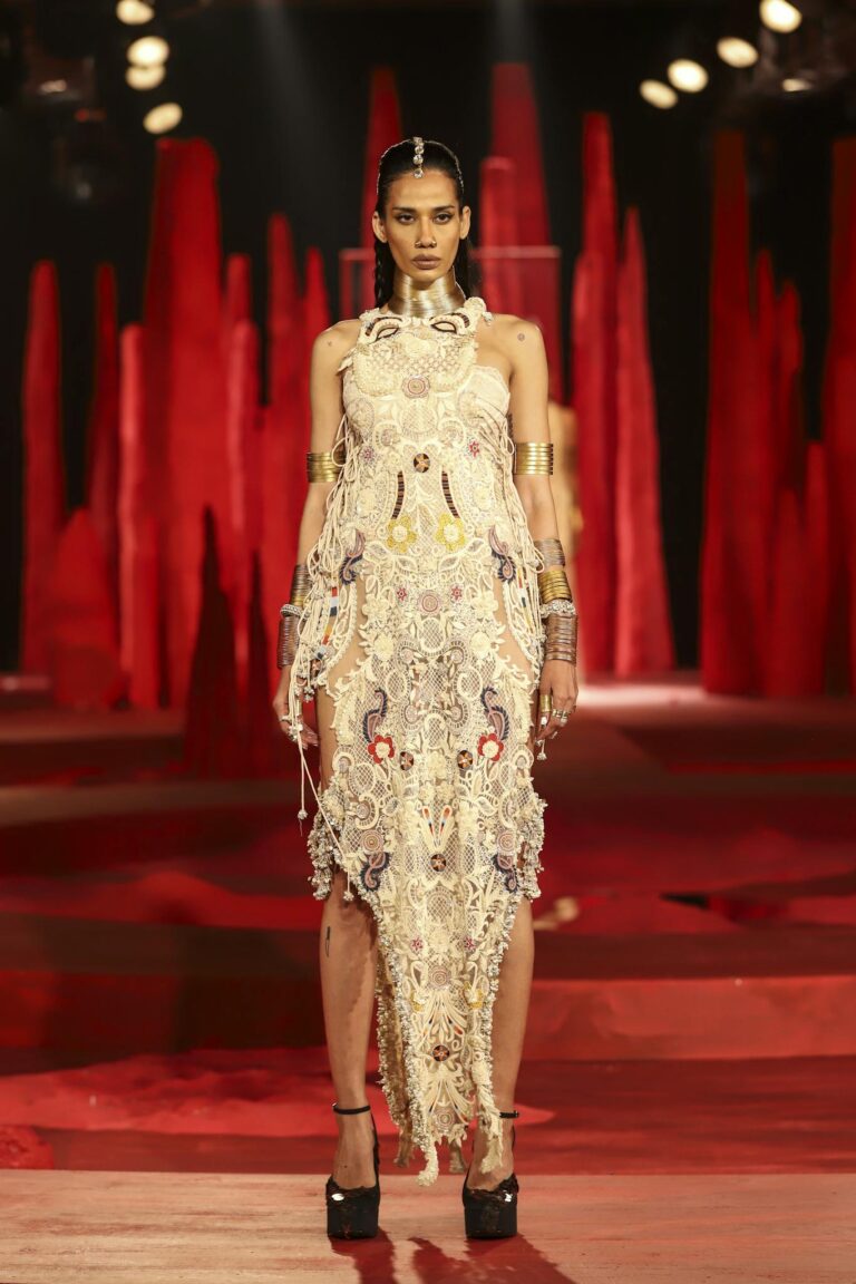 Model walks runway in ornate dress at New Delhi fashion event.